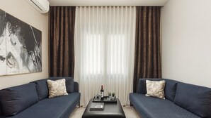 A living room with two dark sofas, a black ottoman, a small table with a bottle, glasses, and a plant. - Anvy Stylish Suites Ioannina (Ioannina)
