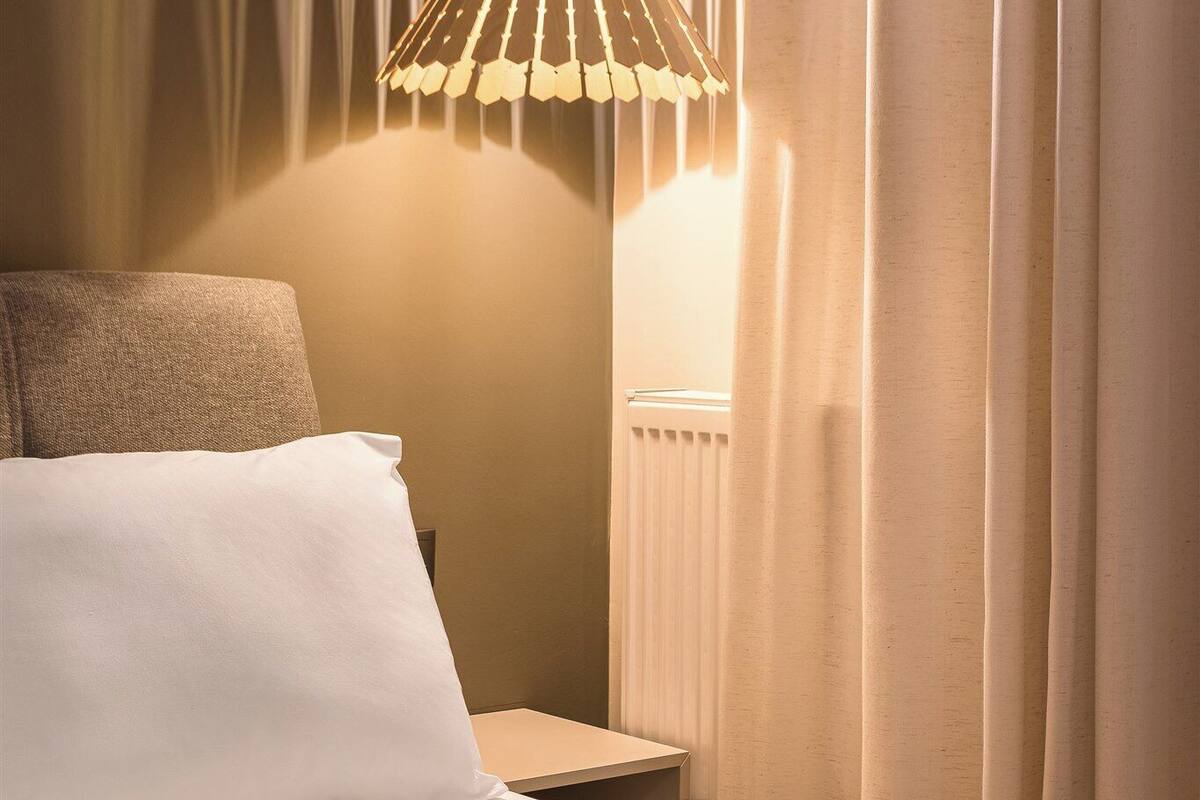 Ein ordentlich bezogenes Bett mit weißen Laken, einer Nachttischlampe und einem Nachttisch.