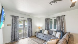 A living room with a grey sofa, a flat-screen TV, and a ceiling fan.