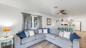 A modern living room with a grey sectional sofa, a small white side table, a lamp, and a window with curtains.