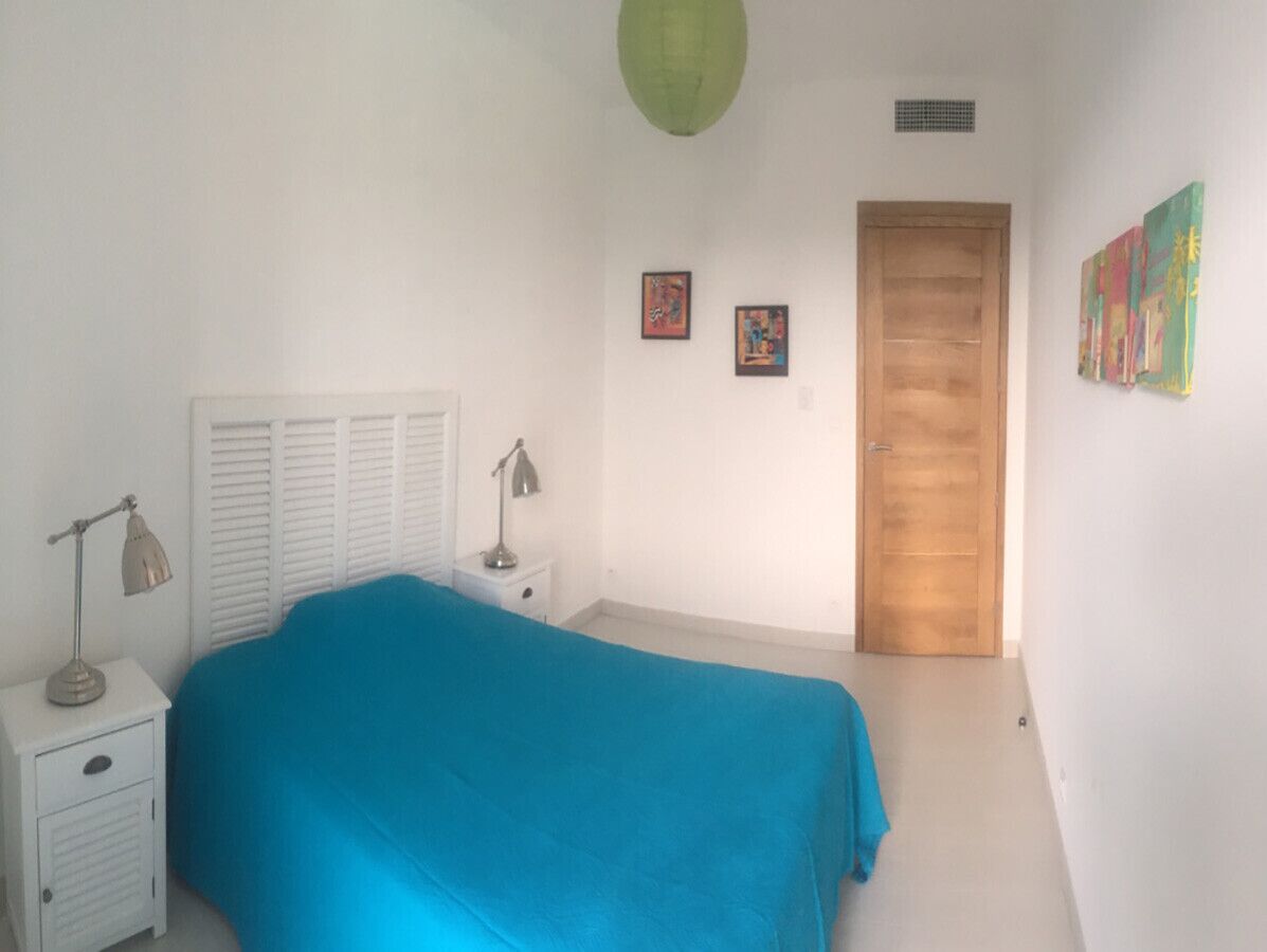 A bedroom with a bed, a nightstand, a lamp, a door, and wall art.