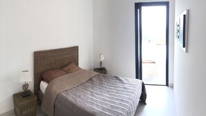 Ein Schlafzimmer mit Bett, Nachttischen, einer Lampe und einer Tür zu einem Außenbereich.