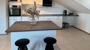 A modern kitchen with a central island, two stools, and a microwave above the oven.