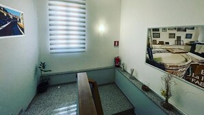 Une petite pièce étroite avec une fenêtre, un extincteur, une plante et un tableau encadré accroché au mur.