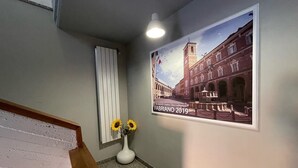 Un couloir orné d’une affiche représentant un bâtiment historique, d’un vase blanc contenant des tournesols et d’un escalier en bois.