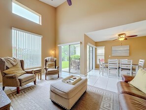 A spacious living area with a sofa, armchair, ottoman, and dining set.