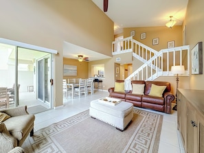 A spacious living room with a staircase, a dining area, and a kitchen in the background.