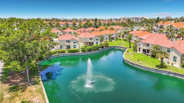 A residential area with a central pond, houses with red roofs, and palm trees.