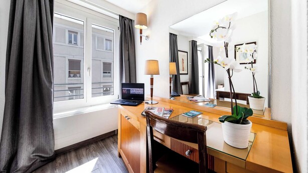 A hotel room with a wooden desk, a laptop, a lamp, a mirror, and a potted plant. - Cosy, Air-conditioned Flat -1br/4p- Geneva (Geneva)