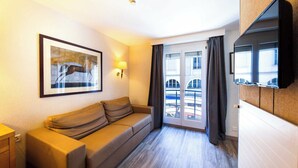 A hotel room with a sofa, a framed picture on the wall, a flat-screen TV, and a view through the glass door. - Cosy, Air-conditioned Flat -1br/4p- Geneva (Geneva)