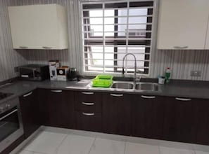 A kitchen with dark cabinets, a stainless steel sink, a microwave, and a window with blinds. - 3 Bedroom En-suite House in Communication Hills, East Legon Hills, Accra (Santeo)