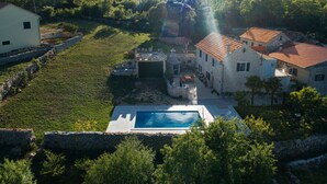 A stone villa with a swimming pool, surrounded by lush greenery and hills. - Holiday Home Leptir (Siveric)