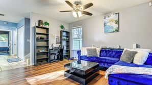 A living room with a blue sofa, a glass coffee table, wooden flooring, a ceiling fan, and a bookshelf. - 4 Mi to Dtwn Jacksonville: Game Day Escape! (Jacksonville)