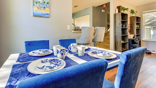 A dining area with a table set for four, blue chairs, and a painting on the wall. - 4 Mi to Dtwn Jacksonville: Game Day Escape! (Jacksonville)