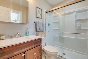 A bathroom with a wooden vanity, a white sink, a toilet, and a glass-enclosed shower. - 11 Mi to Mercedes-benz Stadium: Home w/ Yard! (Conley)
