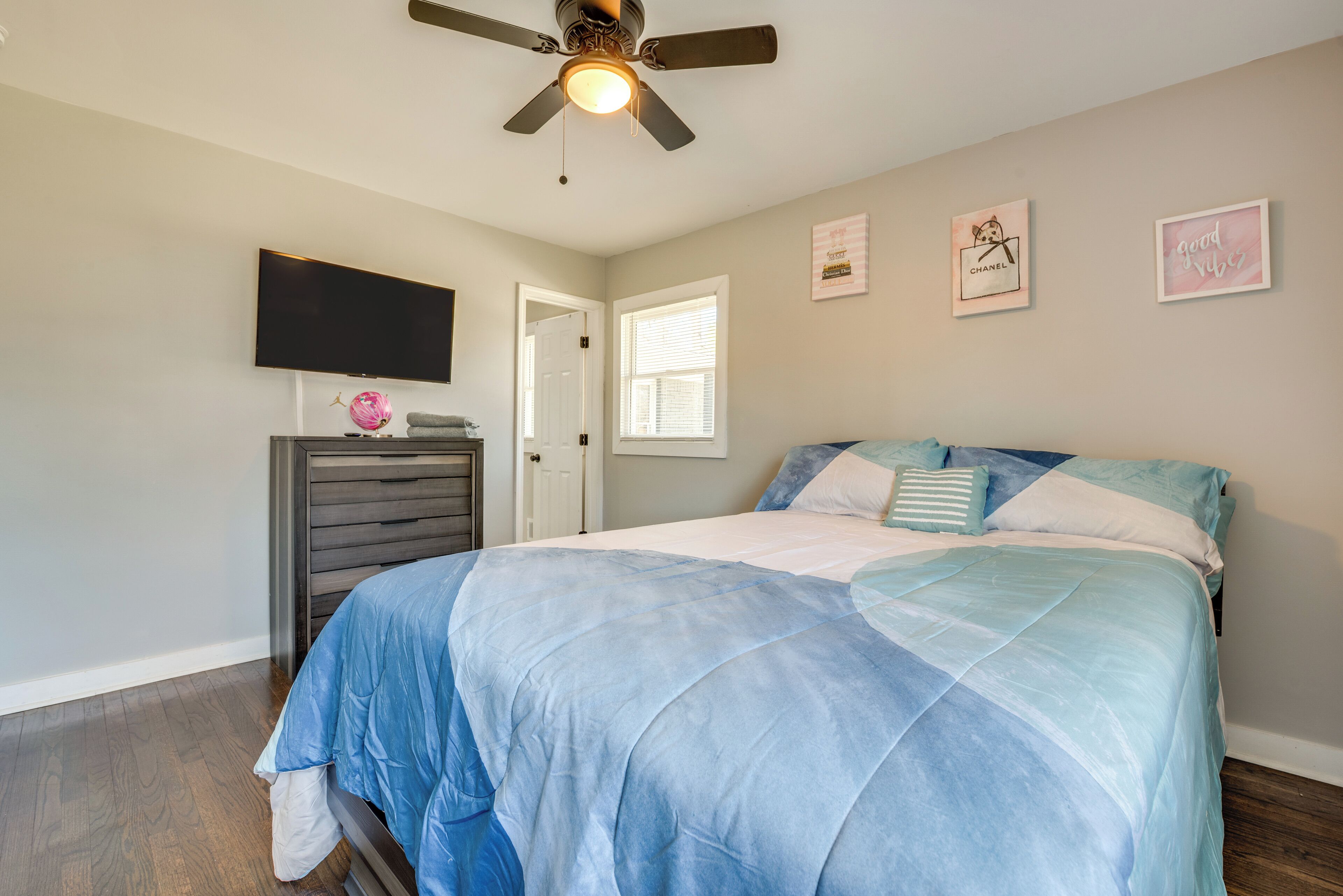 A bedroom with a bed, a ceiling fan, a TV, a dresser, and a window.