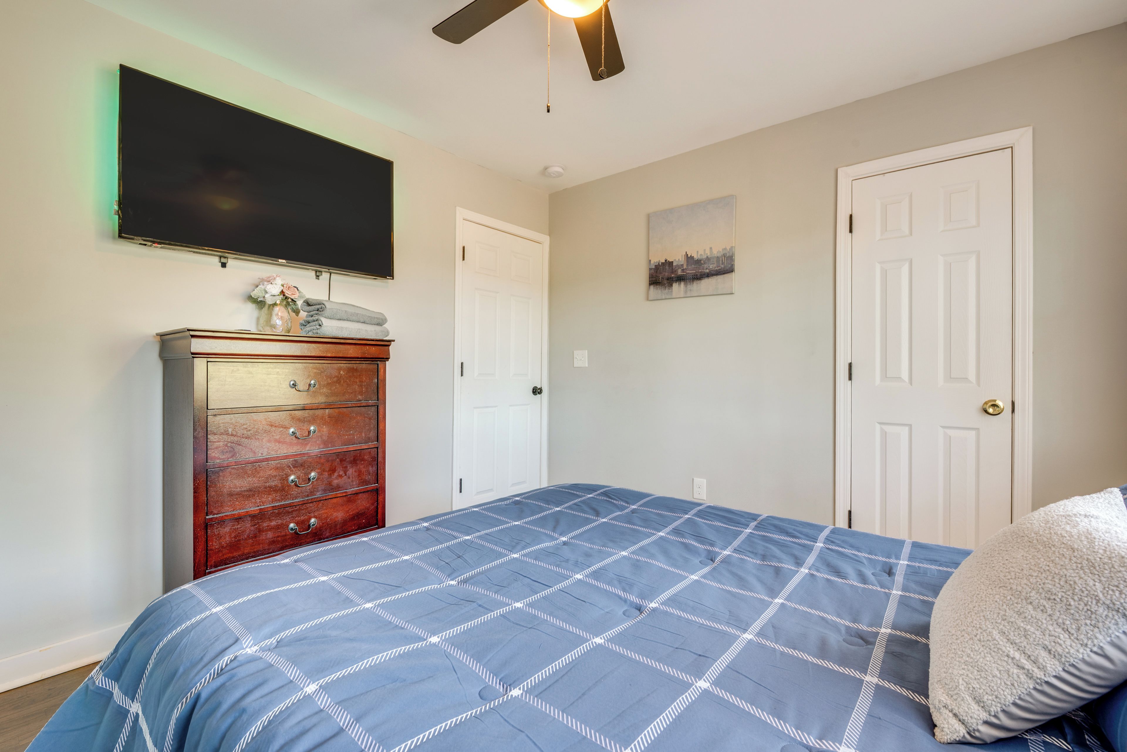 A bedroom with a bed, a dresser, a flat-screen TV, and two doors.