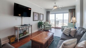 Una sala de estar con televisor de pantalla plana, una mesa de centro de madera, un sofá y un sillón. Hay un balcón con vistas.