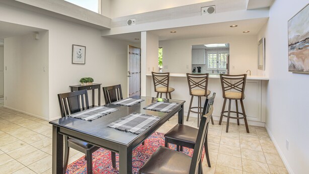 A dining area with a long table, six chairs, and a kitchen in the background. - Palm Desert Condo w/ Community Perks: WFH Friendly (Palm Desert)