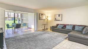 A living room with a large grey rug, a brown leather sofa, and a dining area with chairs and a table. - Palm Desert Condo w/ Community Perks: WFH Friendly (Palm Desert)