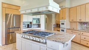 Une cuisine moderne dotée d’un îlot central, d’appareils électroménagers en acier inoxydable et de meubles de rangement en bois.