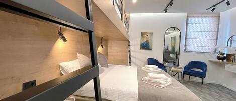 Quarto de hotel moderno com beliches, uma escrivaninha, uma cadeira e um espelho.