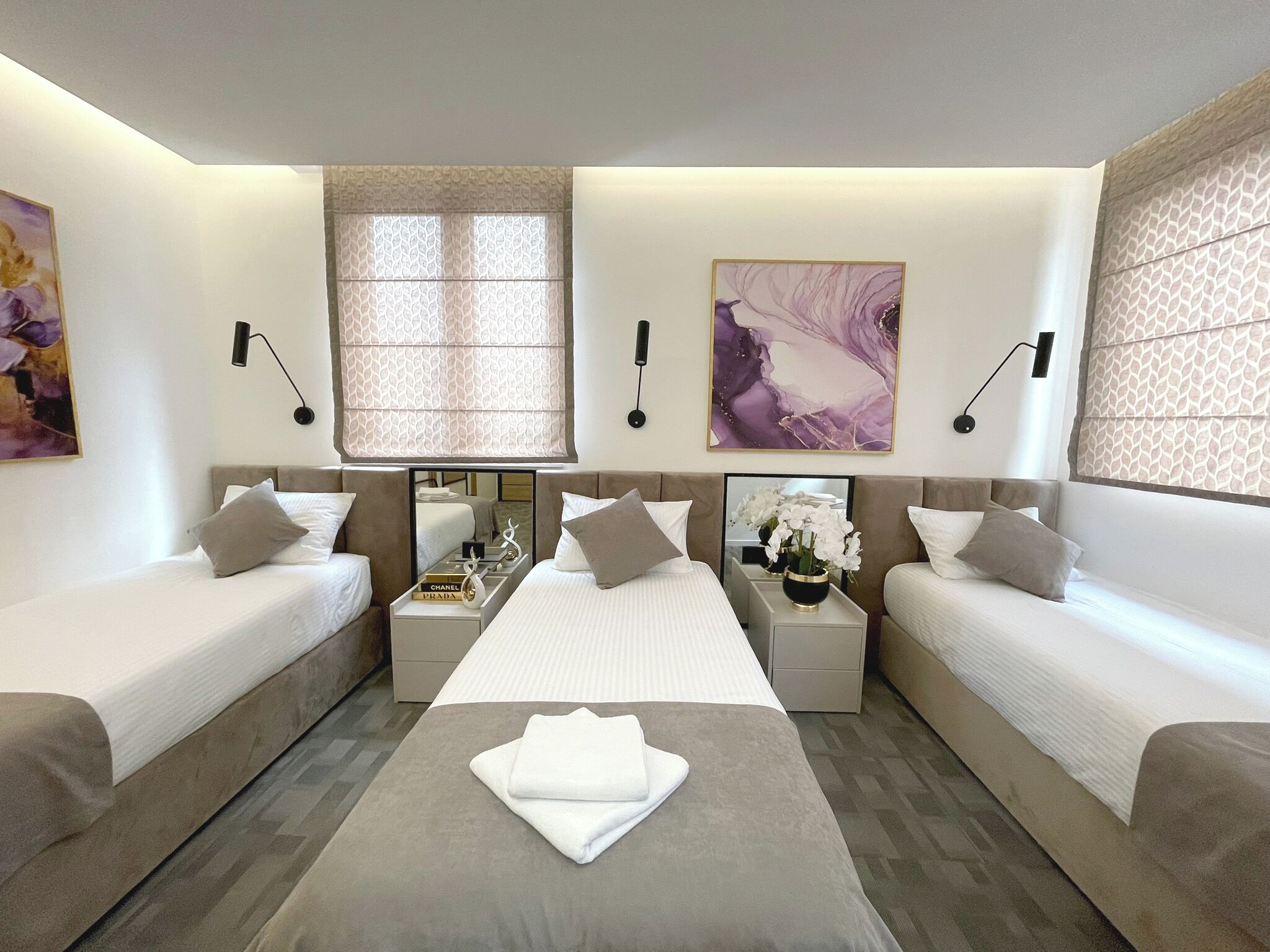 Habitación de hotel moderna con dos camas individuales, una cama doble en el centro, una mesita con una toalla y obras de arte en las paredes.