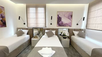 Habitación de hotel moderna con dos camas individuales, una cama doble en el centro, una mesita con una toalla y obras de arte en las paredes.