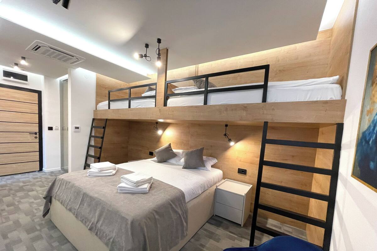 Ein Schlafraum mit Etagenbetten, Schreibtisch, Stuhl, einer Treppe und einem Bild an der Wand.