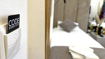 Una camera d'hotel con un letto, un comodino e uno specchio. Sulla parete, un cartello con la scritta 'CODE BUSINESS HOTEL'.