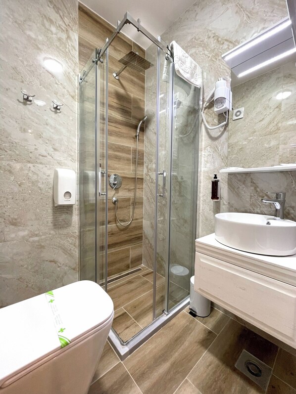 A modern bathroom with a glass-enclosed shower, a white sink, and a toilet. - Hotel NPL CODE (East Sarajevo)