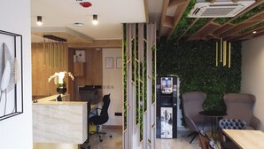 Un espace de bureau moderne comprenant un comptoir d’accueil, un fauteuil de bureau noir, un fauteuil de salon gris et un climatiseur fixé au mur.