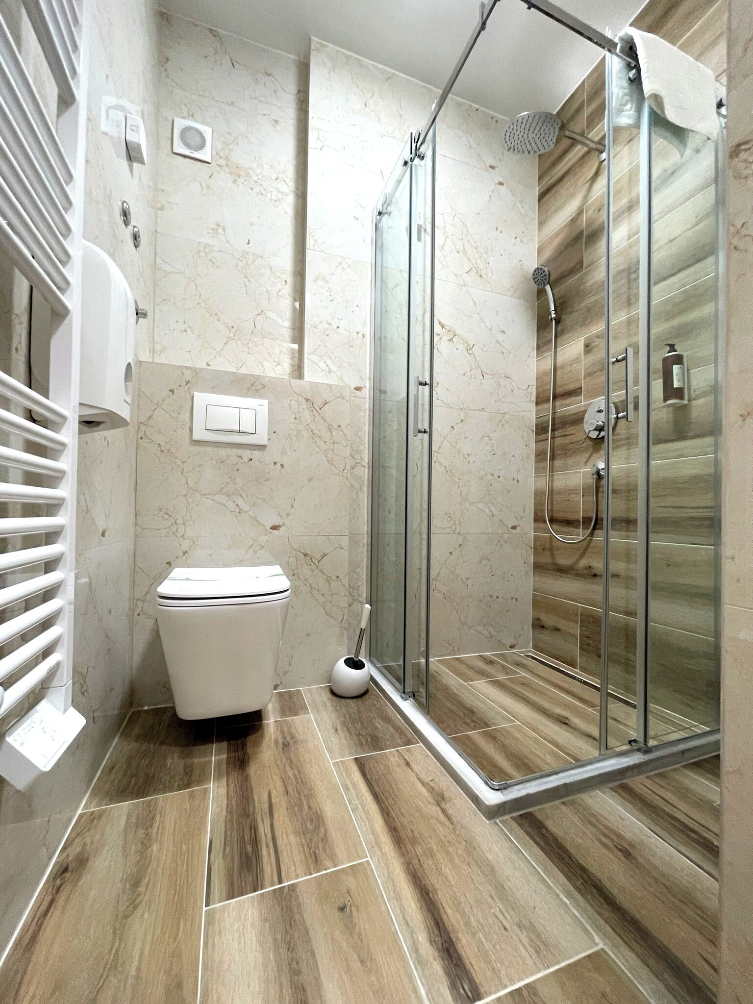 A modern bathroom with a glass-enclosed shower, a toilet, and a hand dryer.