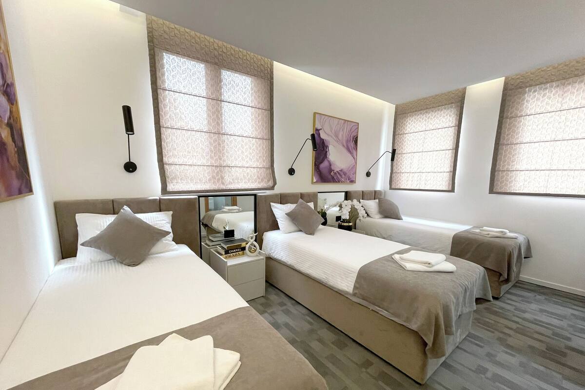 Ein Hotelzimmer mit zwei Betten, einem Nachttisch und einem großen Fenster mit gemusterten Vorhängen.