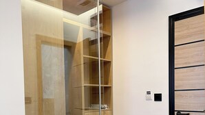 Un placard moderne doté de portes coulissantes en verre, d’étagères intégrées et d’une porte noire avec une poignée.