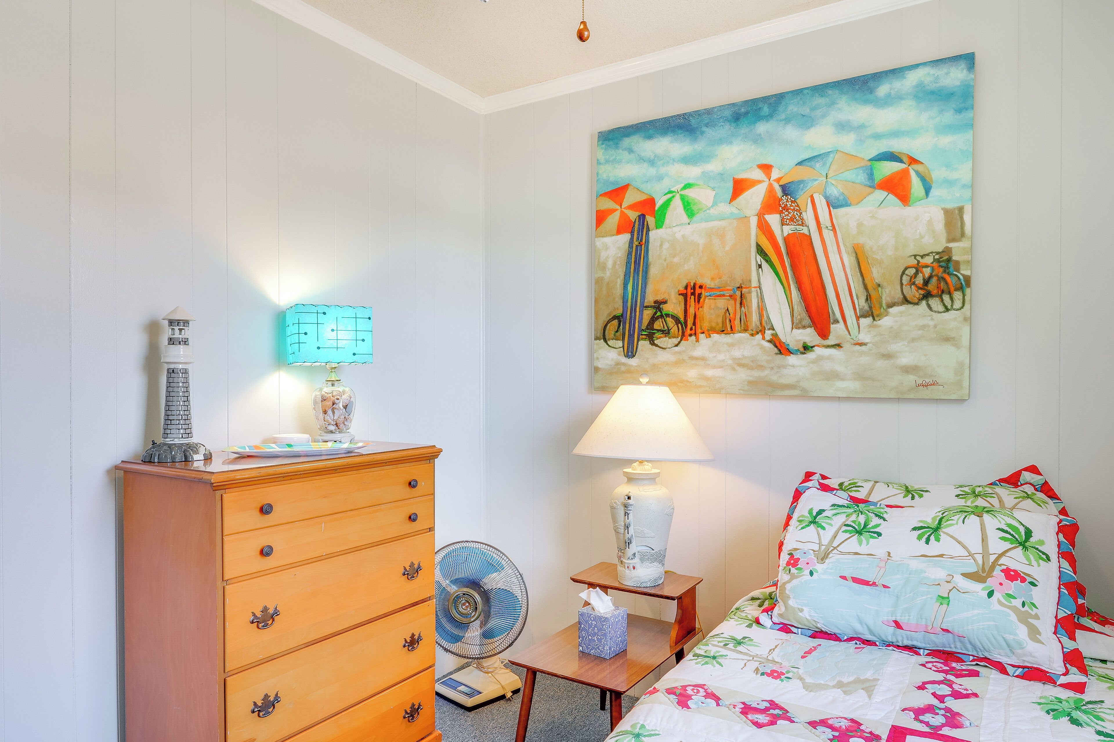 Une chambre à coucher avec un lit, une commode, une lampe et un tableau représentant des parasols de plage.