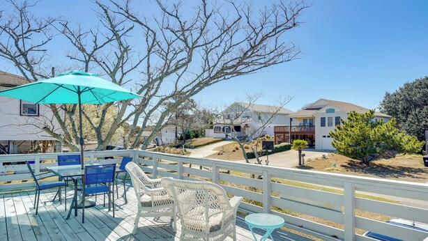 Une terrasse en bois, agrémentée de mobilier d’extérieur, notamment des chaises et une table, qui offre une vue sur un quartier résidentiel avec ses maisons et ses arbres.