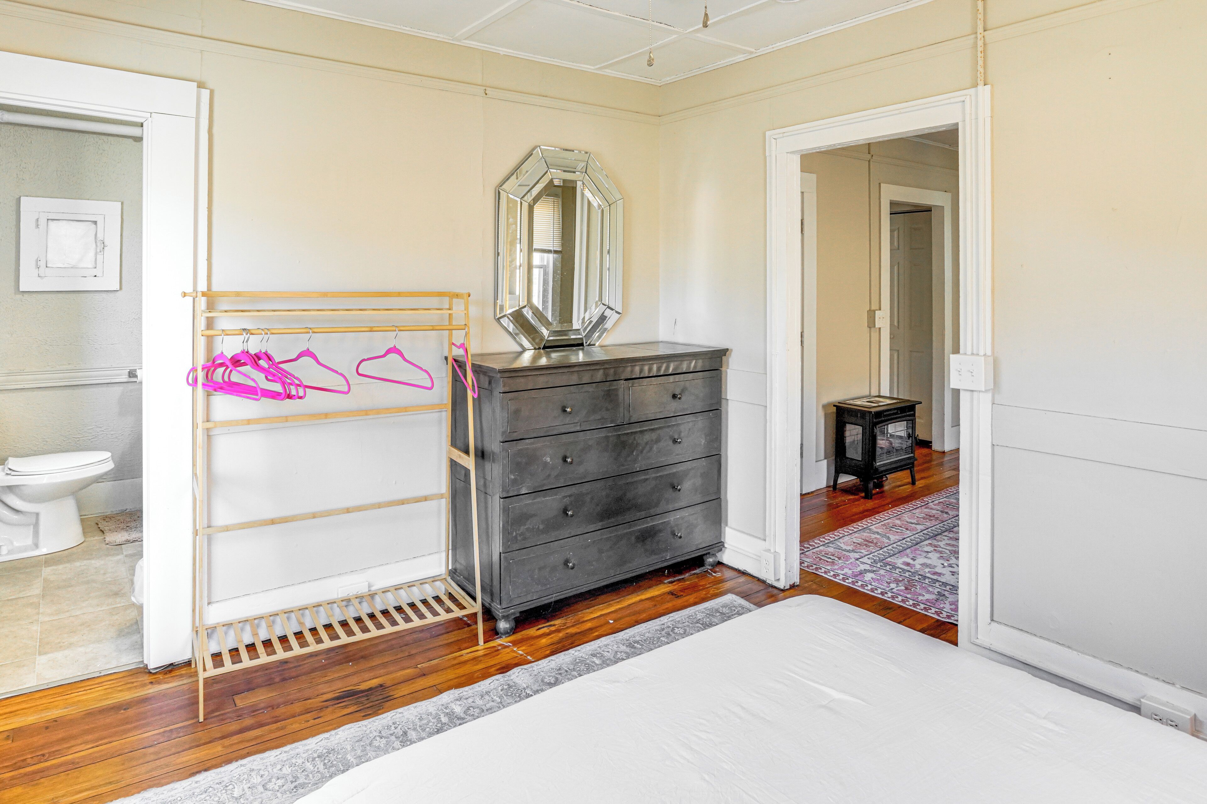 Un dormitorio con suelo de madera, una cama, un aparador y un espejo.