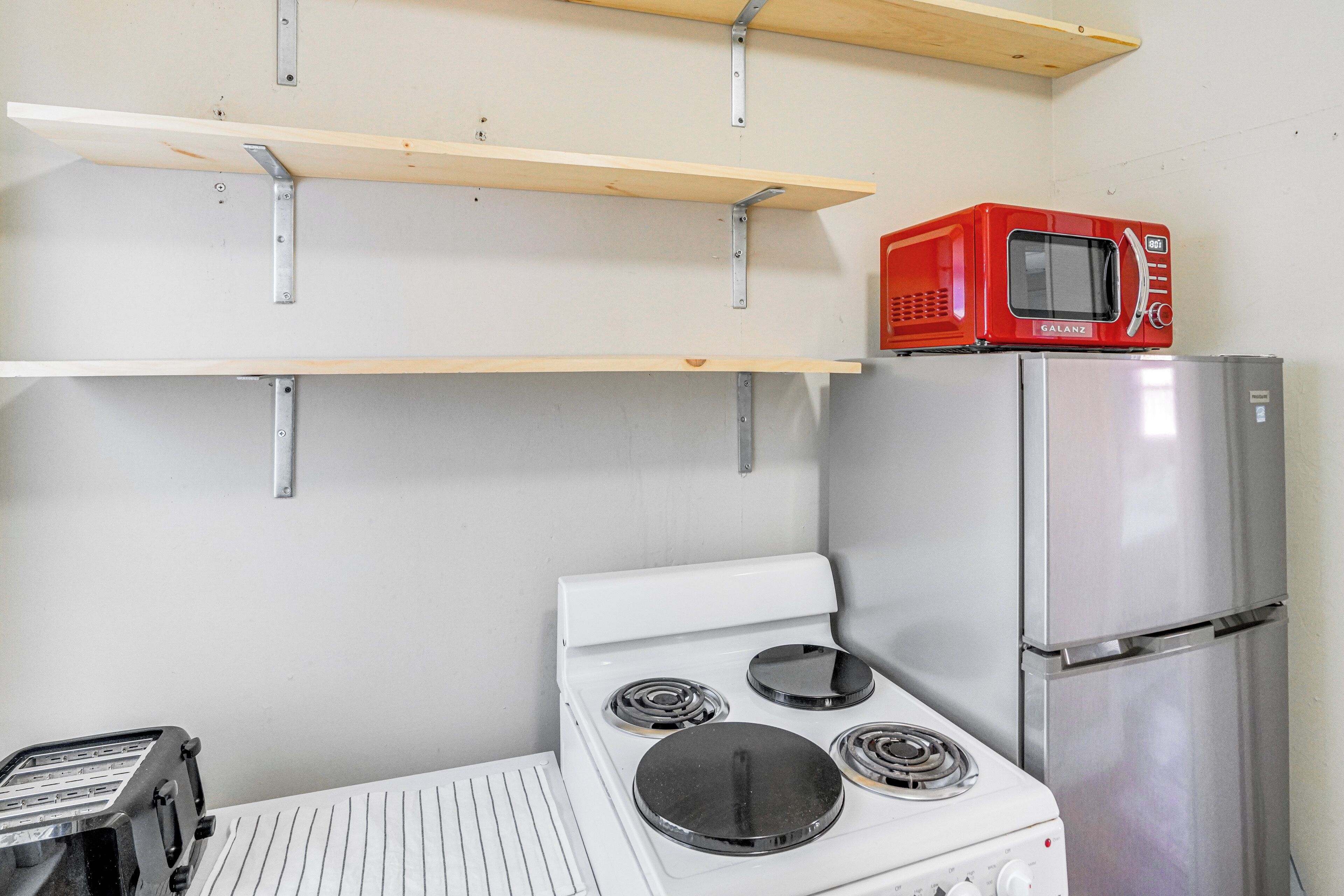 Une cuisine avec un four blanc, un réfrigérateur en acier inoxydable, un micro-ondes rouge et des étagères en bois.
