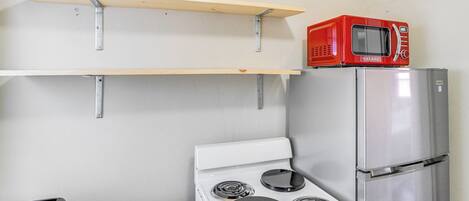 Une cuisine avec un four blanc, un réfrigérateur en acier inoxydable, un micro-ondes rouge et des étagères en bois.