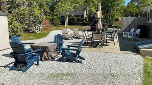 An outdoor seating area with Adirondack chairs and a table, surrounded by a gravel patio. - < 1 Mi to Craigville Beach: Home w/ Patio & BBQ (Centerville)