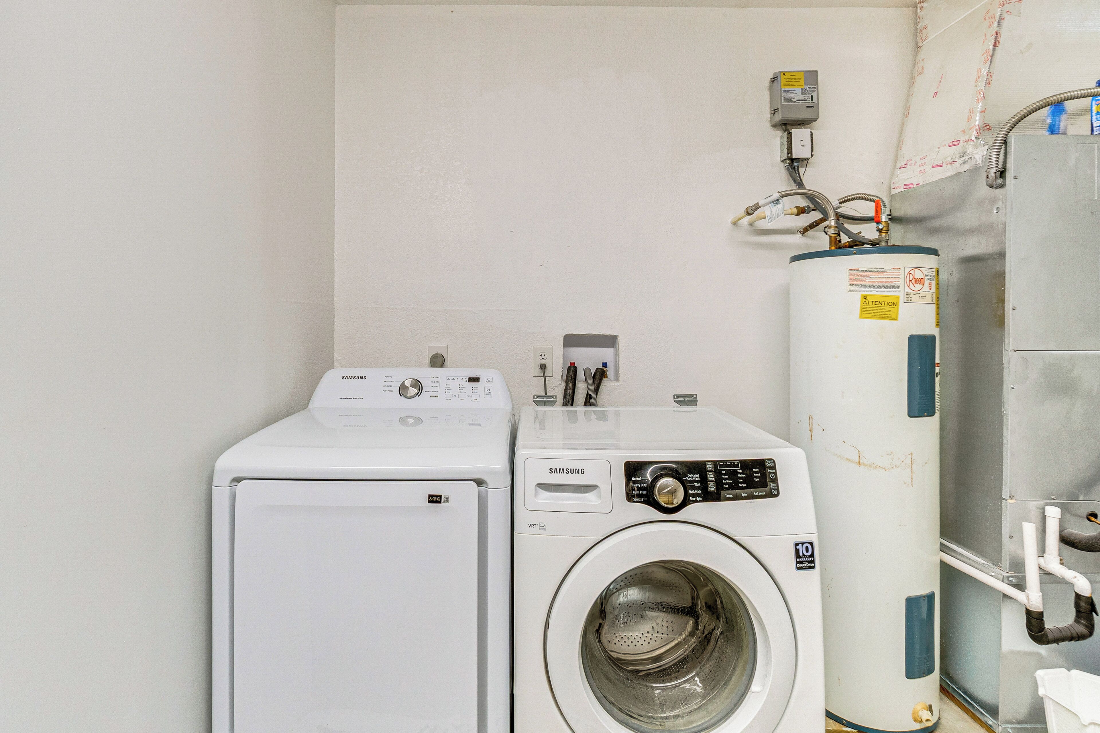 A laundry area with a Samsung washer and dryer, a water heater, and a water tank.