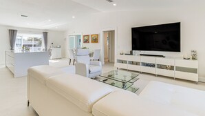 Ein modernes Wohnzimmer mit Glastisch, weißen Sofas, einem Flachbildfernseher und einem minimalistischen Design.