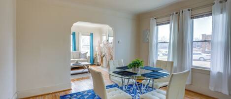 A modern dining area with a glass table, white chairs, and a blue patterned rug.