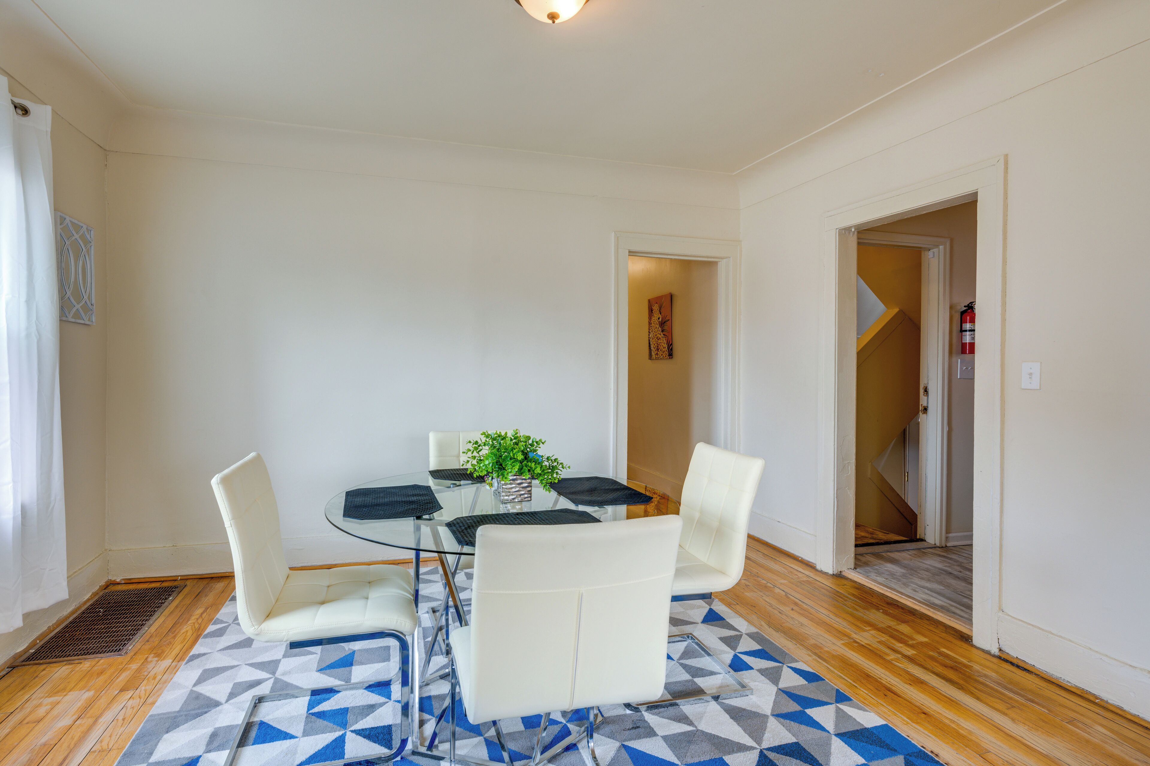 A dining area with a glass table, white chairs, and a patterned rug.