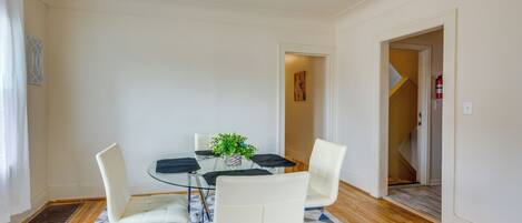 A dining area with a glass table, white chairs, and a patterned rug.