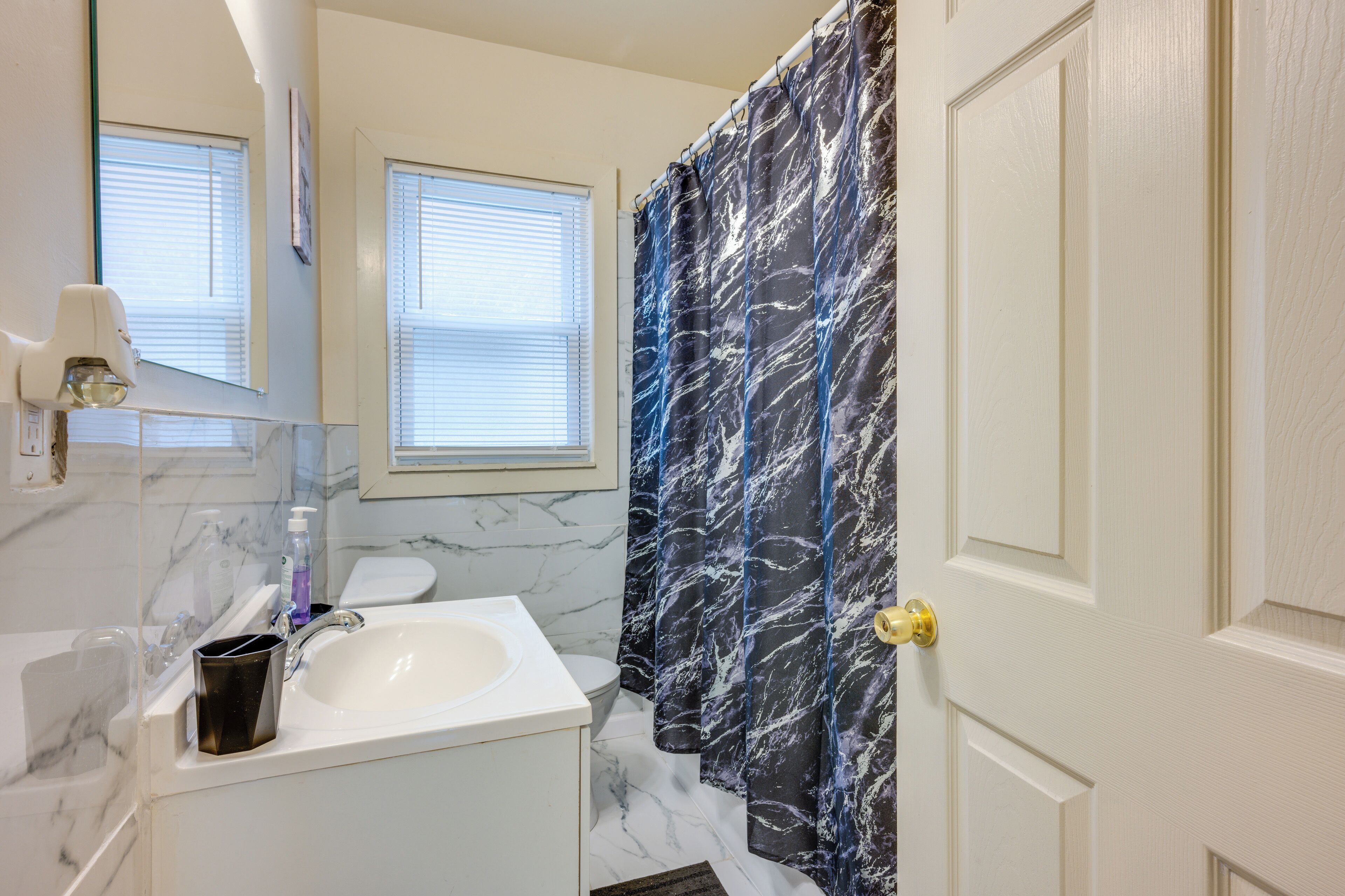 Une salle de bain avec un lavabo blanc, un miroir, des toilettes et un rideau de douche à motif marbré.