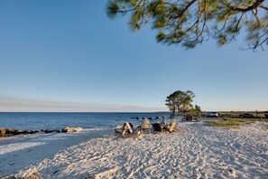 A beach with a row of beach chairs and a wooden structure, likely a barbecue area, near the water.