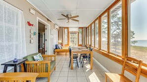 A sunlit dining area with a high ceiling fan, wooden furniture, and large windows offering a view of the beach. - Relax & Refresh: Waterfront Cottage in Panacea (Panacea)