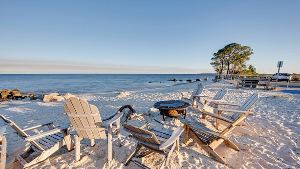 A beach with wooden chairs and a fire pit, surrounded by sand and rocks. - Relax & Refresh: Waterfront Cottage in Panacea (Panacea)